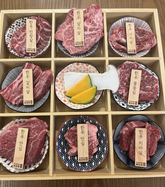 아홉 칸 나무 상자에 접시마다 담은 한우 — 안창살·살치살·새우살·갈비살·꽃등심·안심·치마살 이름표, 가운데 칸은 새송이버섯과 단호박